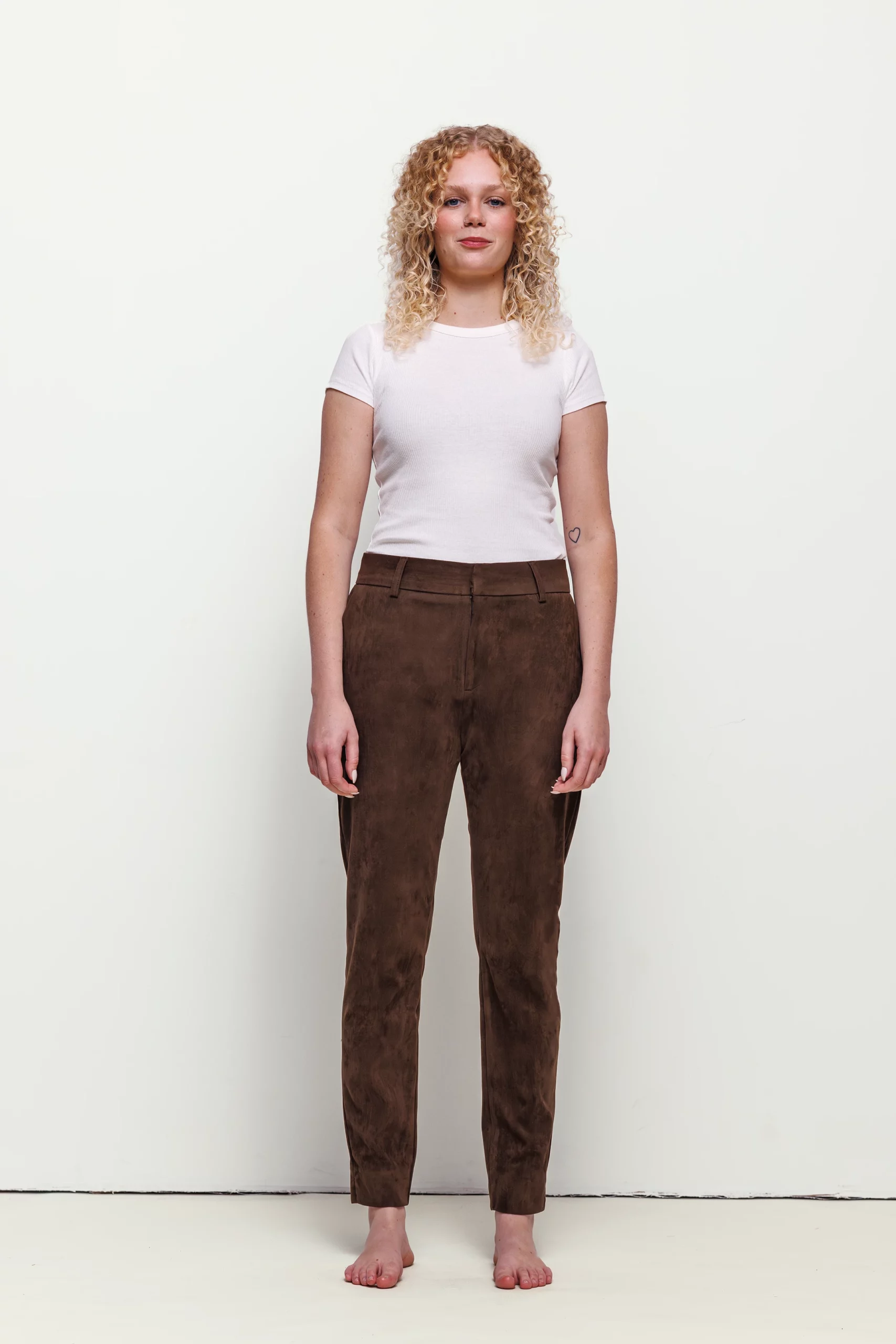 a woman with blonde curly hair wearing brown pants and white shirt