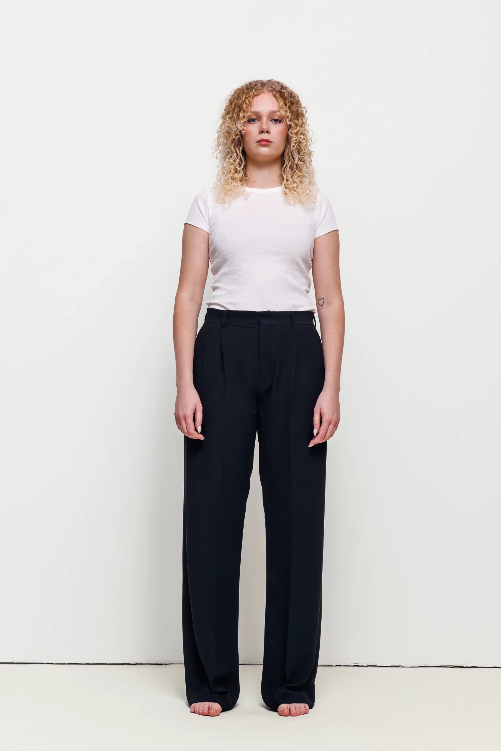 a woman with curly blonde hair wearing black pants and white shirt