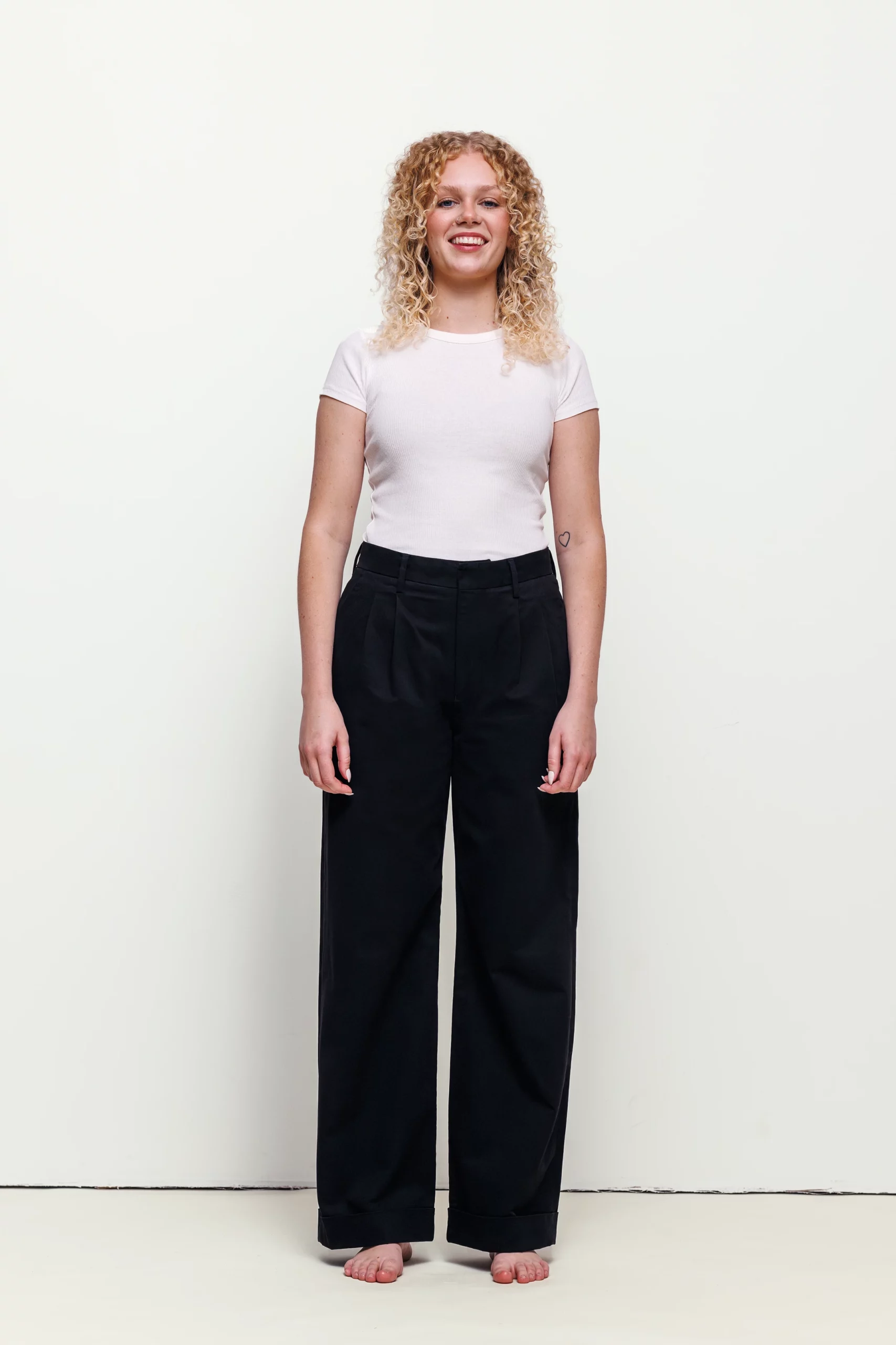 a woman with blonde curly hair wearing black pants and white shirt