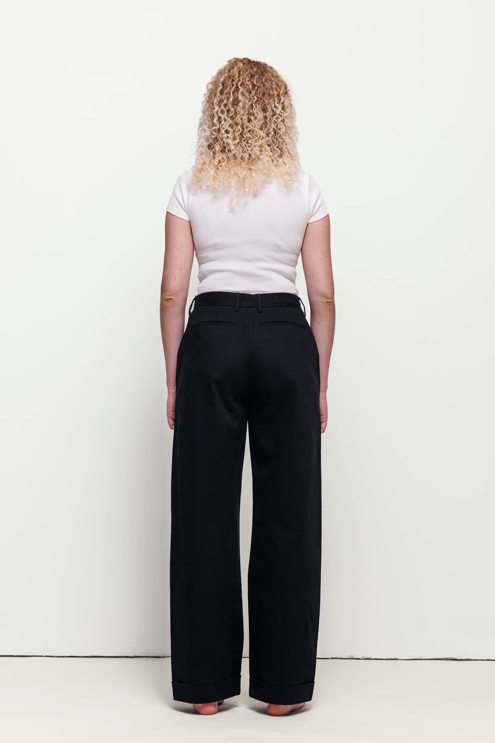 a woman with long curly blonde hair wearing black pants and white shirt