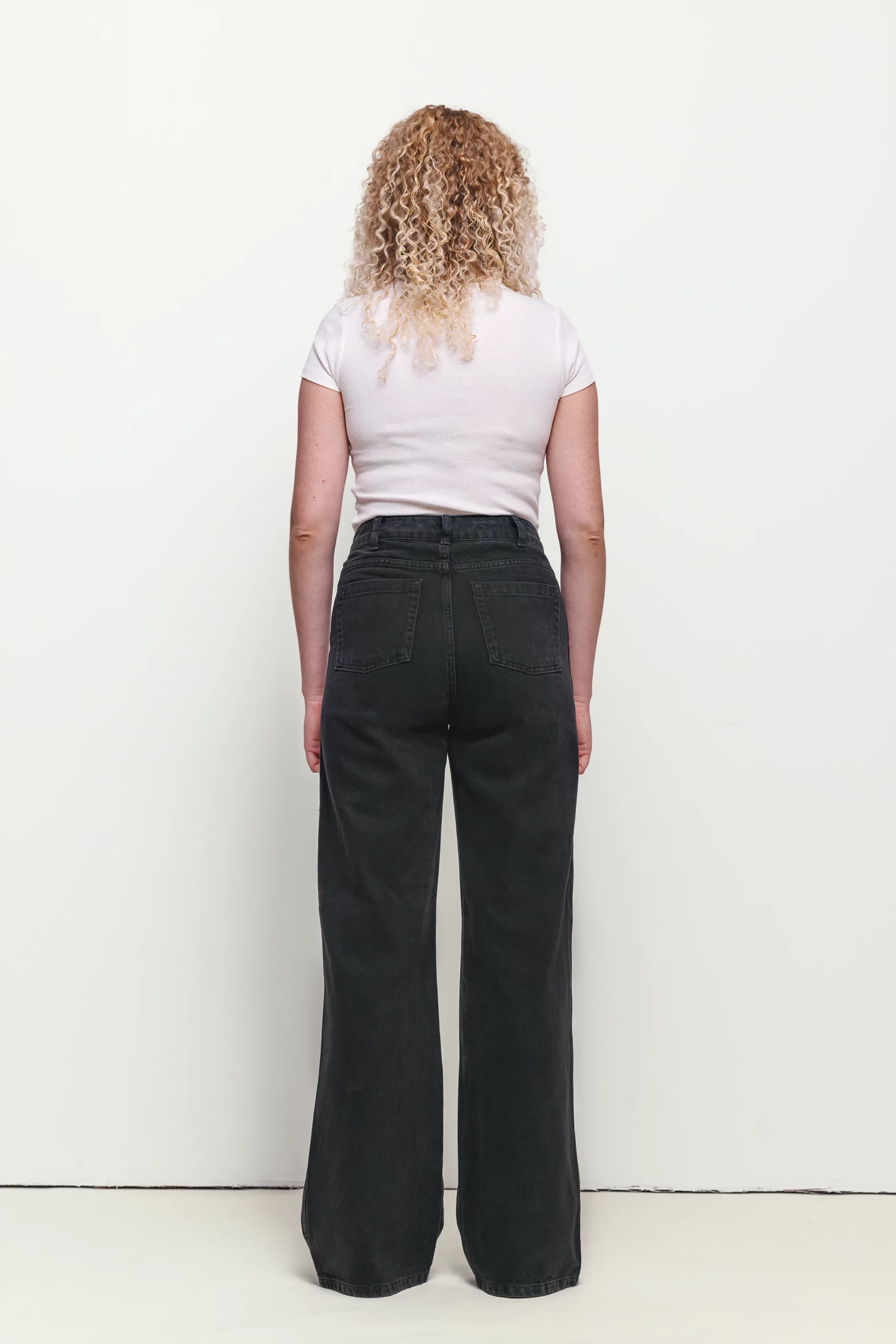 a woman with blonde curly hair wearing black jeans and white shirt