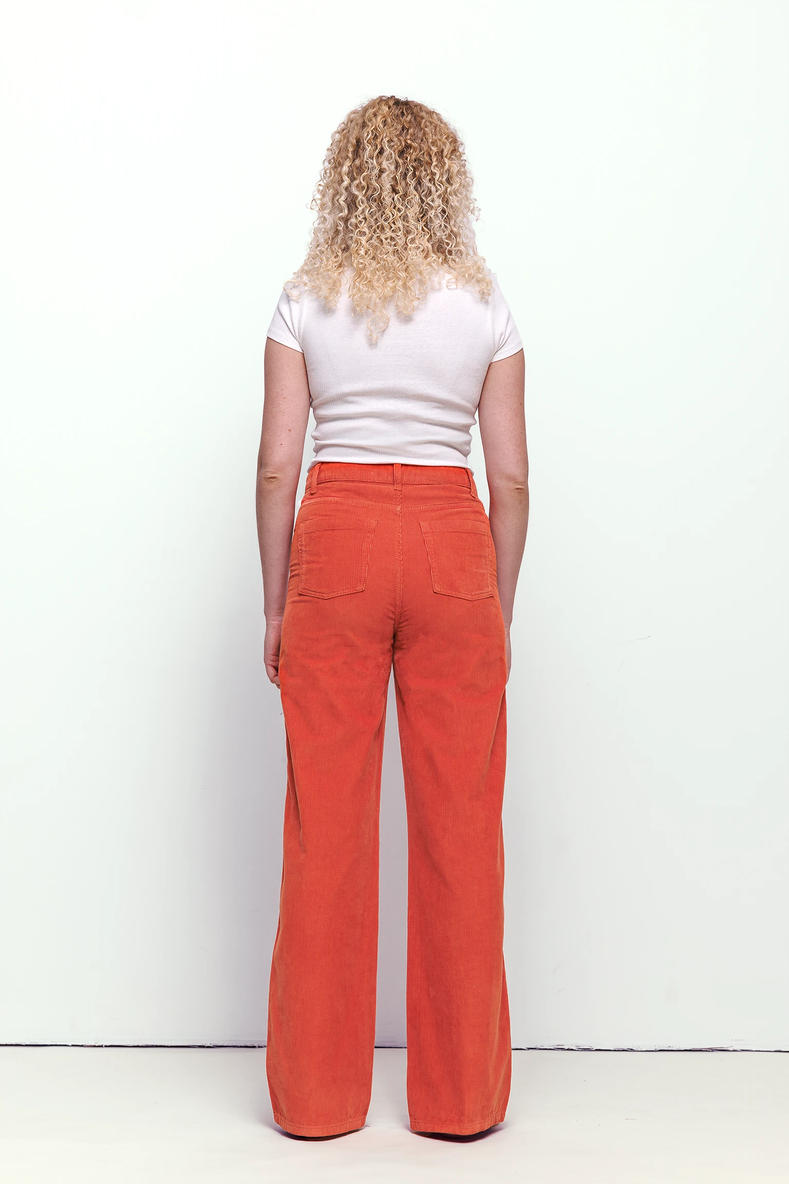 a woman with curly blonde hair wearing orange pants