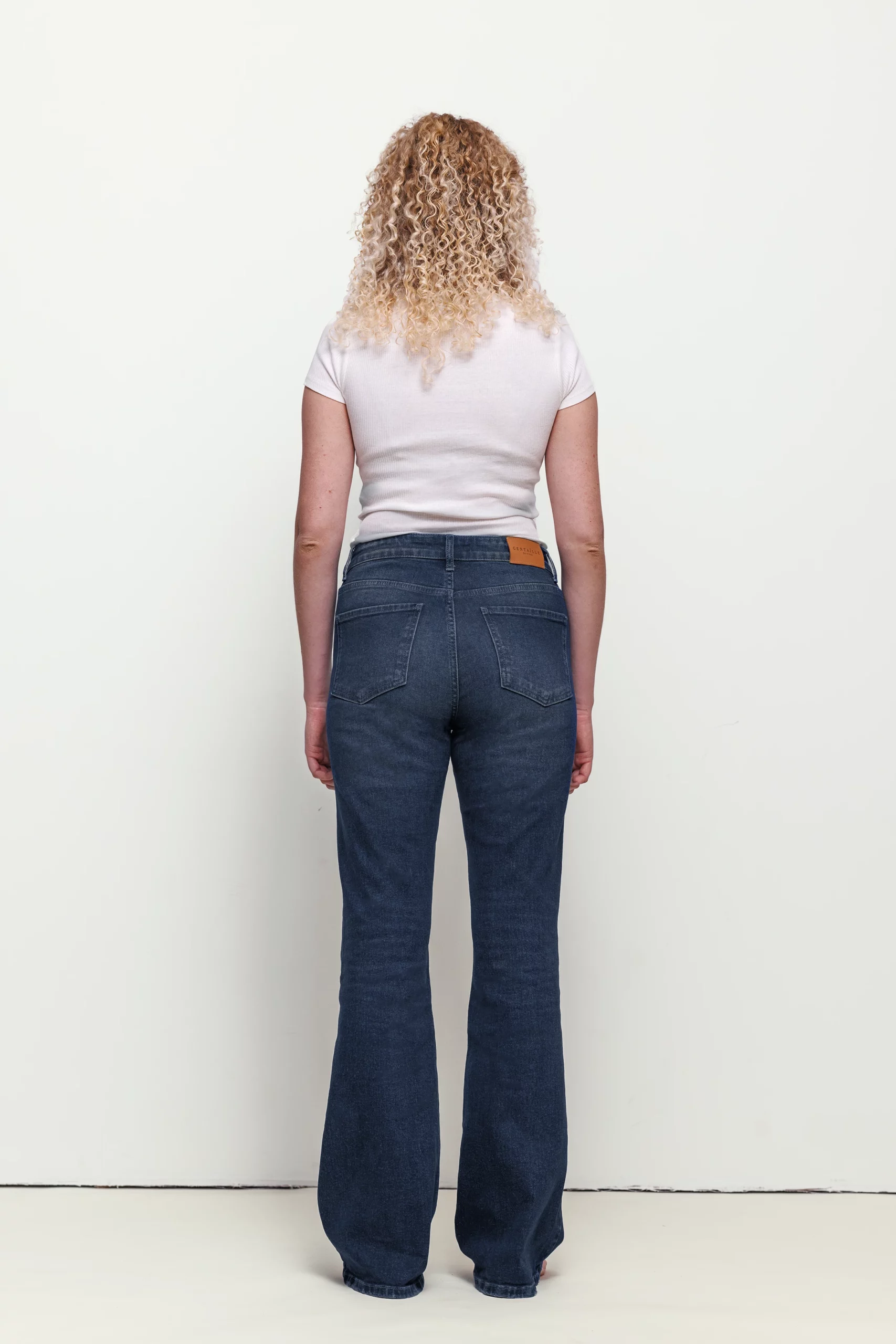 a woman with blonde curly hair wearing blue jeans and white shirt